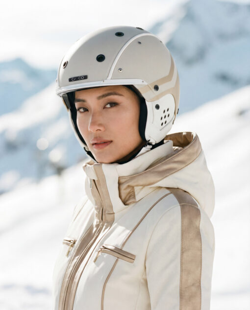 Frau mit cremefarbenem Casco SP-3 Prime Skihelm und weiß-beiger Skijacke vor verschneiter Bergkulisse.